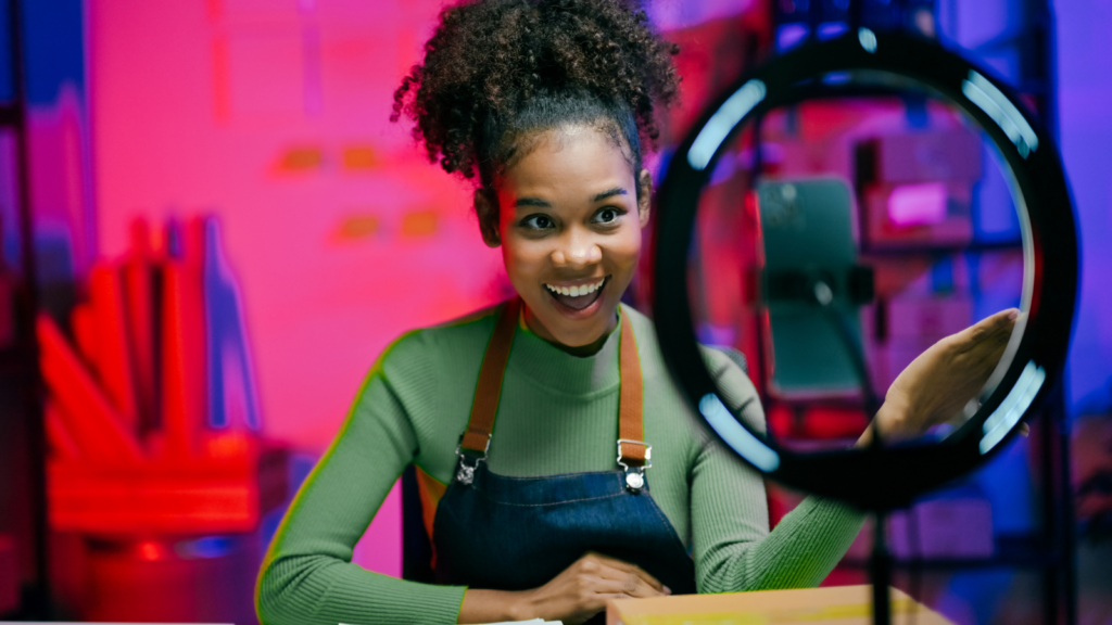 How to find winning TikTok dropshipping products A smiling woman in a green top and apron, behind a ring light, recording on a smartphone.