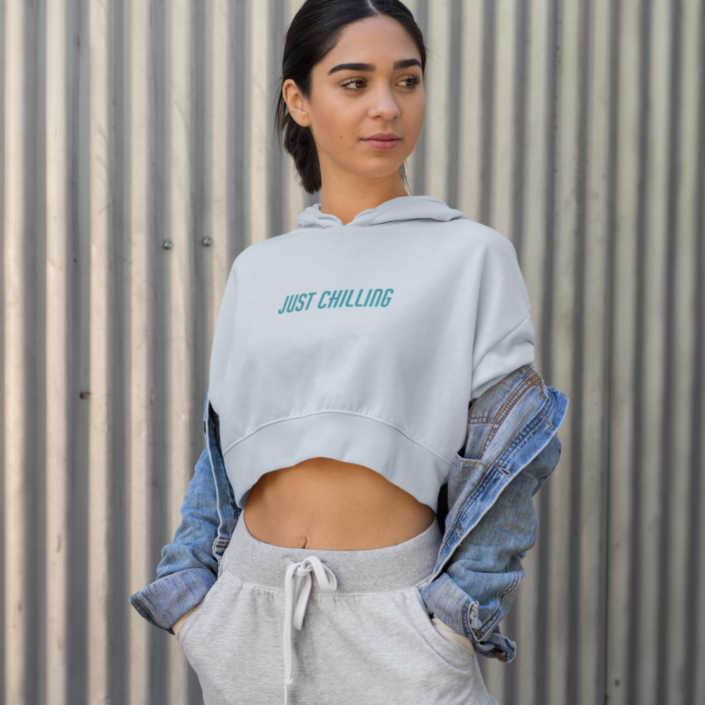 Minimalistic typography A person standing against a corrugated metal wall wearing a white hoodie that says "Just Chilling," a denim jacket, and gray sweatpants.