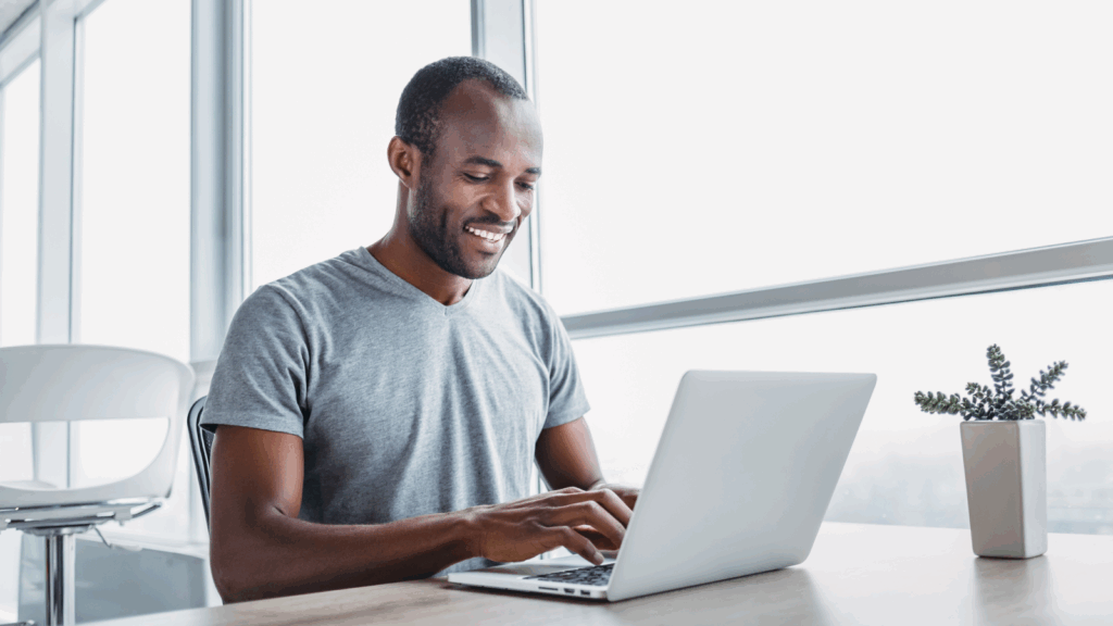 Tools to help you create TikTok content A smiling man sits at a table, working on his laptop with a relaxed demeanor.