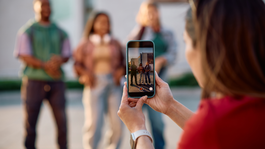 Why TikTok is perfect for dropshipping A person captures a video with a smartphone of three individuals standing outdoors, filming content for TikTok dropshipping.
